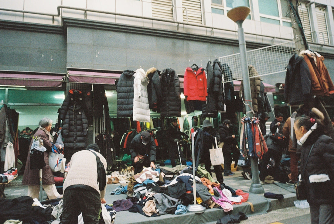 People browsing through racks and piles of clothing at an outdoor street market